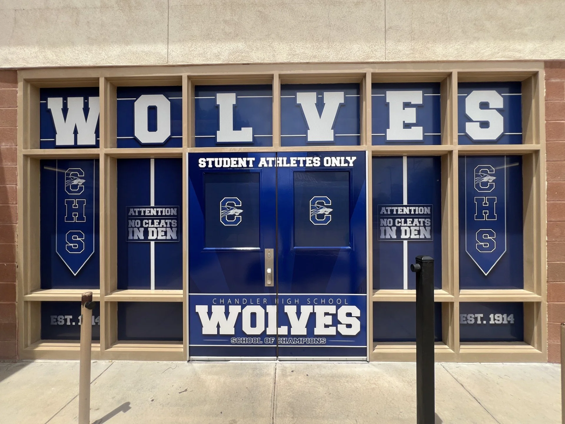 School entrance decorated with signs reading 'WOLVES', 'CHANDLER HIGH SCHOOL', 'SCHOOL OF CHAMPIONS', and 'EST. 1914'. The signs feature the Chandler High School mascot and logo, with two banners on each side of the door.