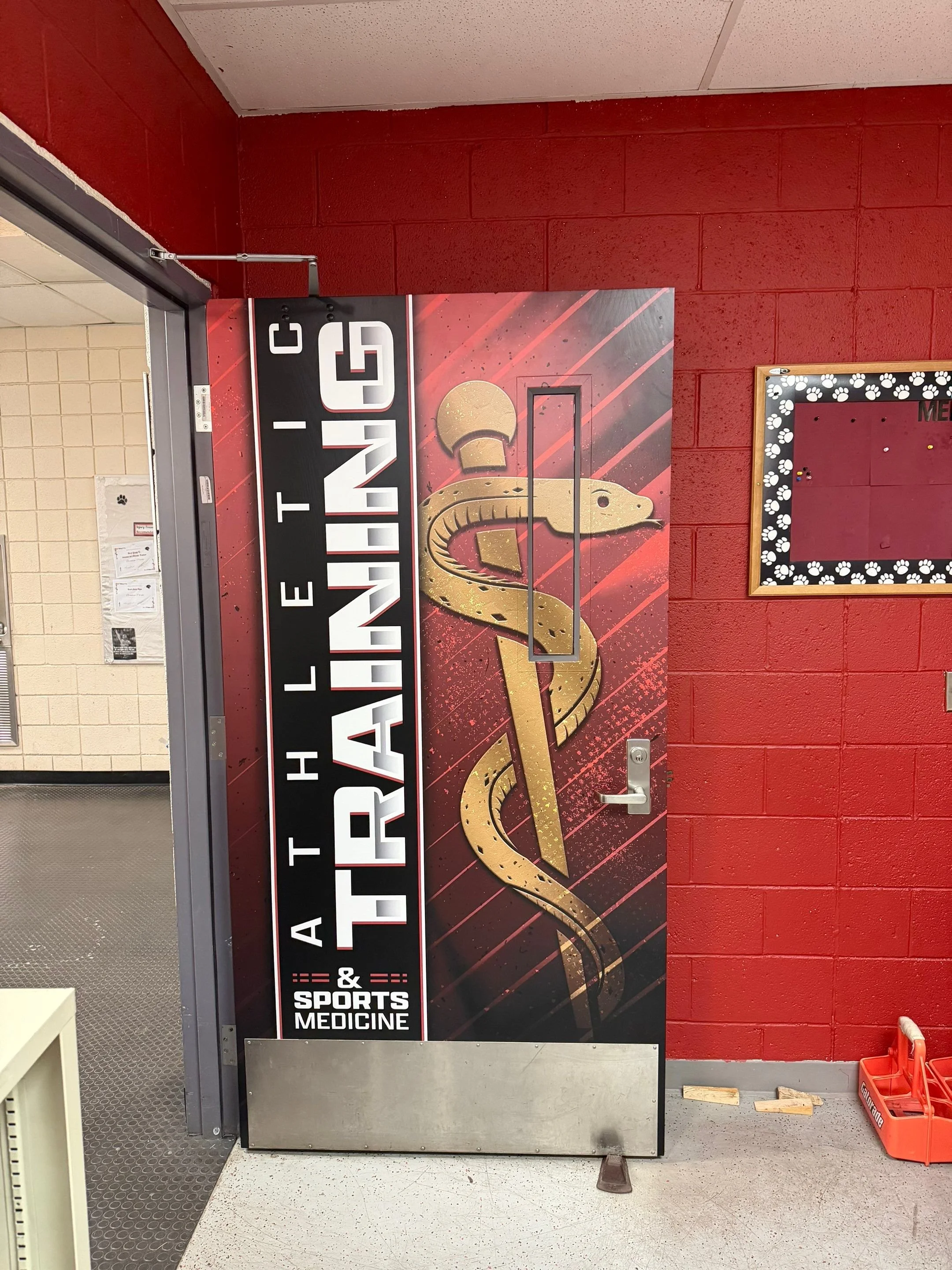 Sign for a sports medicine and athletic training facility with a red and black background, featuring a stylized snake wrapped around a staff, and reading 'ATHLETIC TRAINING & SPORTS MEDICINE.'