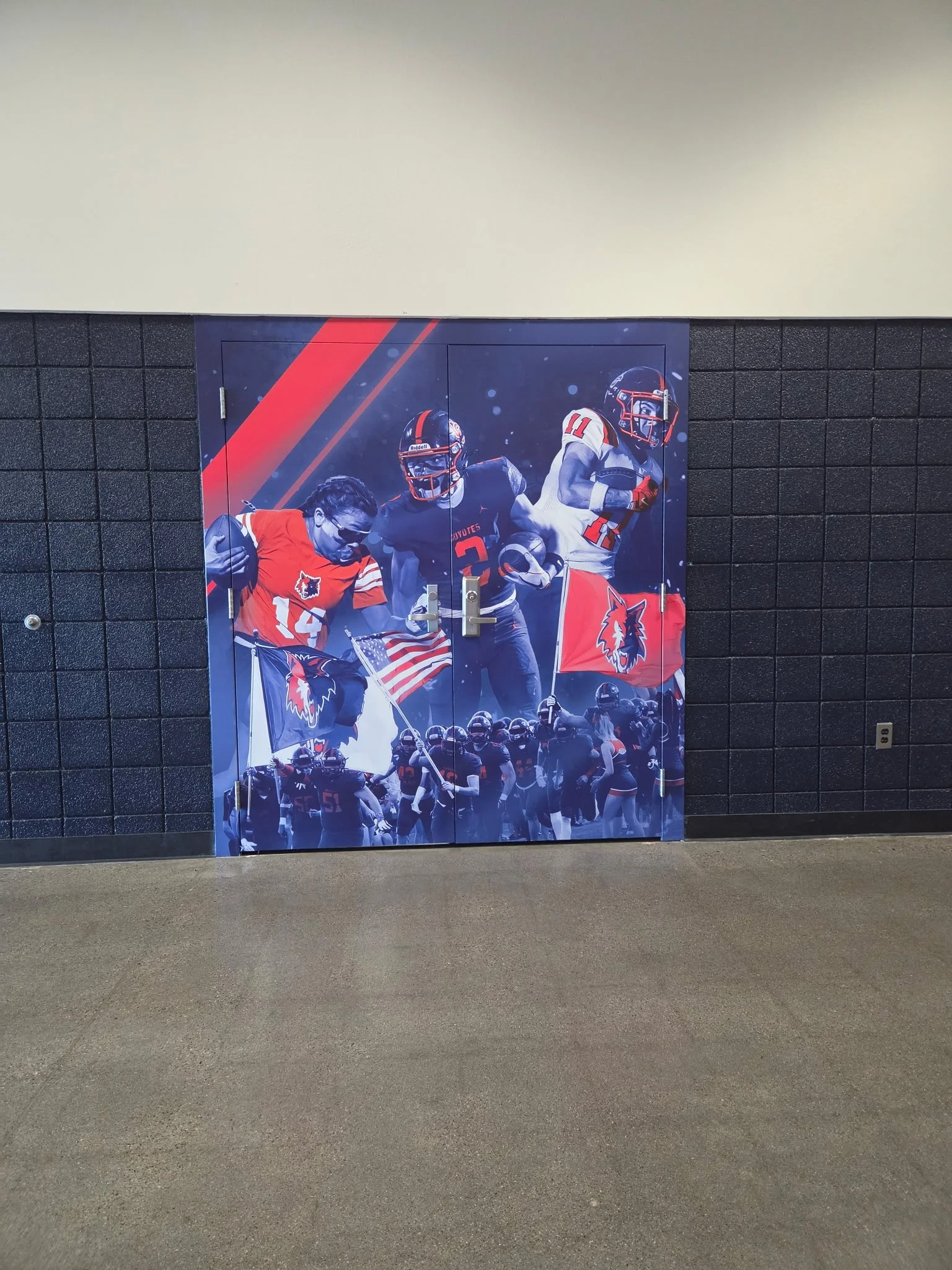 Large poster on a dark wall featuring American football players in red, white, and black uniforms, with some holding flags and football equipment, with a crowd of cheerleaders at the bottom.