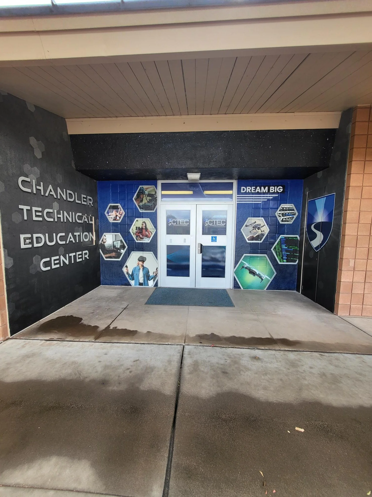 Entrance to a building with a sign for the Chandler Technical Education Center, blue and black decor, and images of technology and education on the wall.