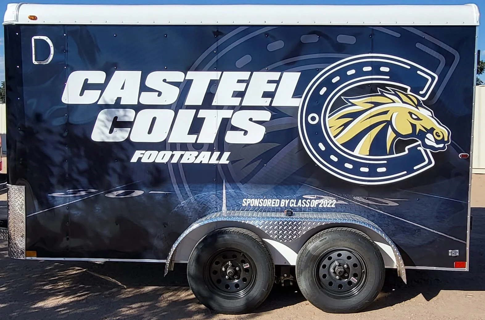 A trailer with a dark blue background featuring the logo of the Castel Colts football team, including a stylized horse head inside a circular emblem, and text indicating the team is sponsored by the class of 2022.
