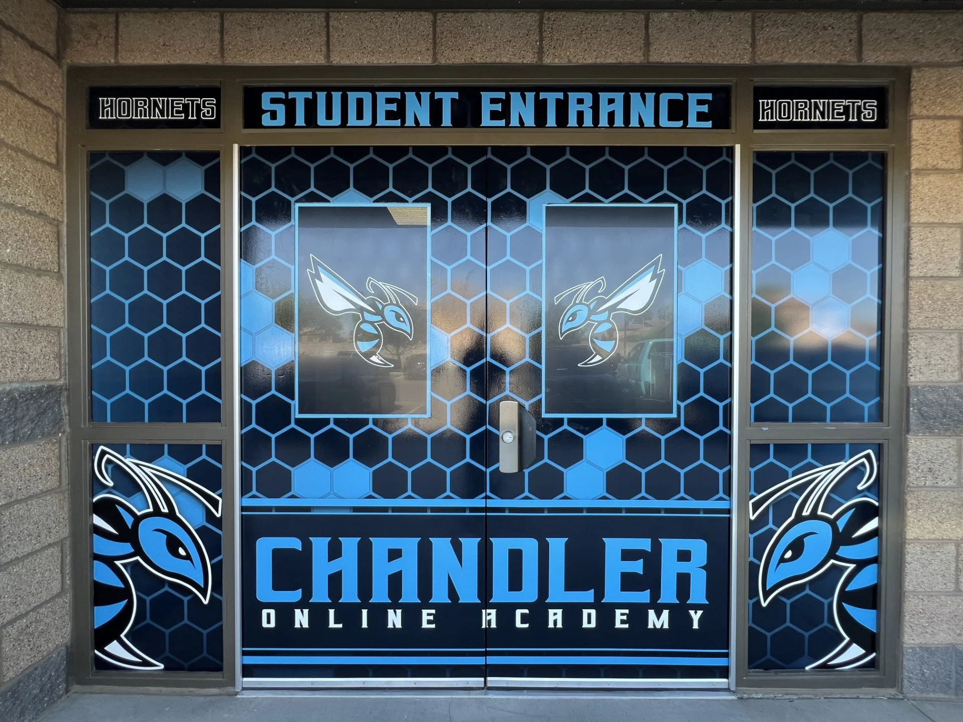Door with sign reading 'Student Entrance' and 'Hornets' logos, and a background pattern of blue hexagons, part of an educational or sports facility.