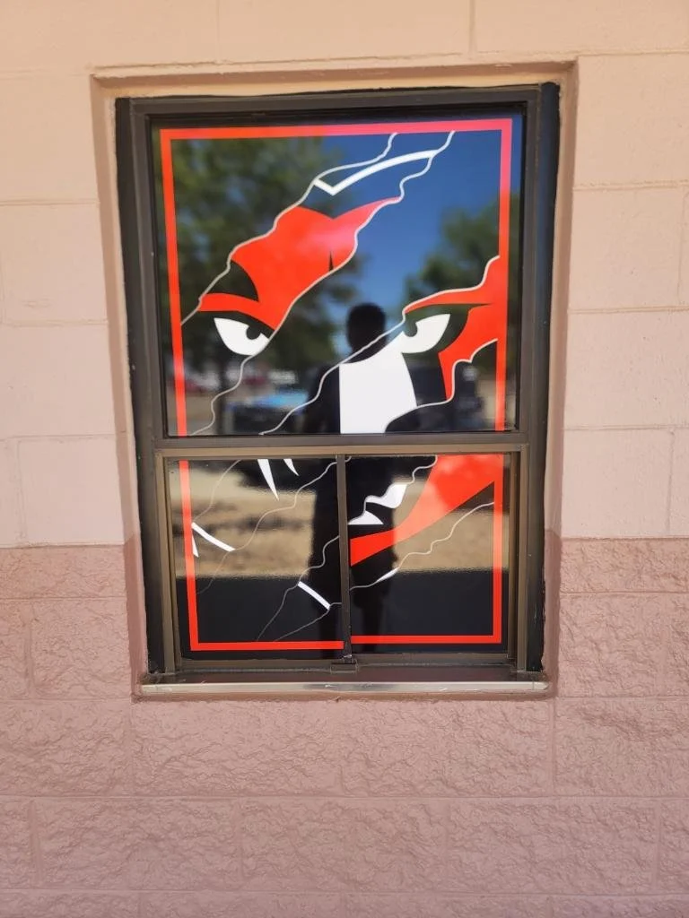 Window decal of a fierce-looking animal face, possibly a panther or wolf, with piercing eyes in red, black, and white colors, on a building's exterior wall.