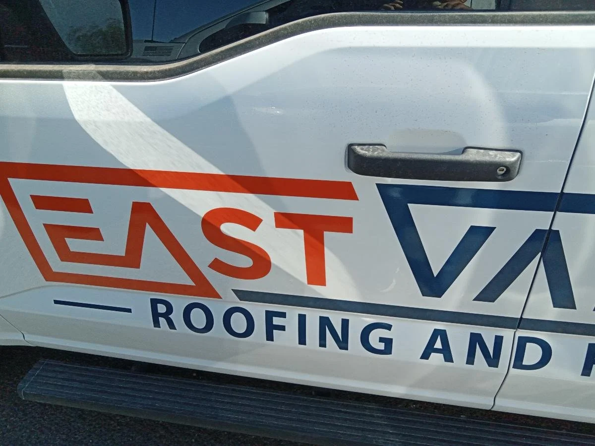 Close-up of a white truck with logo and text for a roofing and siding company, showing part of the side door and handle.