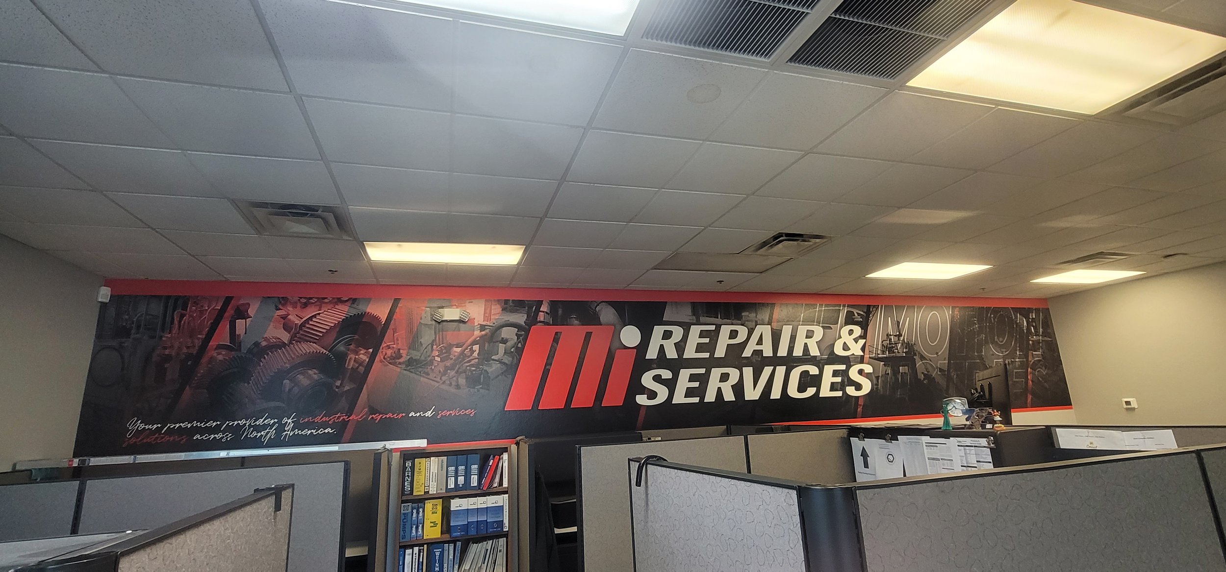 Office cubicles with a banner on the wall reading 'Repair & Services' and images of gears and industrial equipment.
