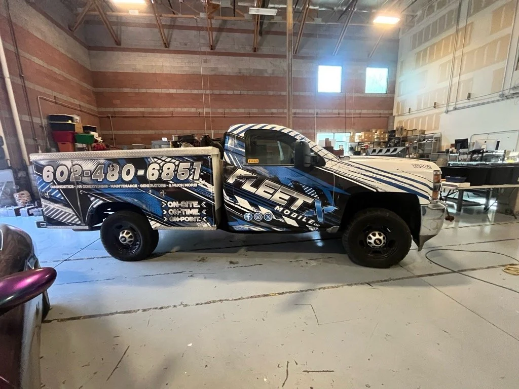 A black and white truck with blue accents inside a warehouse, branded with the logo 'TLE TX Mobile,' a phone number, and text indicating services like on-site, on-time, and on-point.