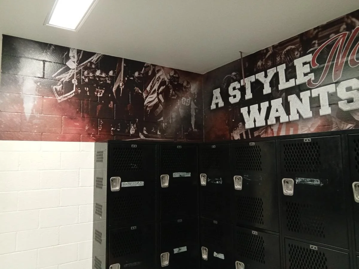Locker room with black lockers and a mural of football players and the words "A STYLE WANTS" on the wall.