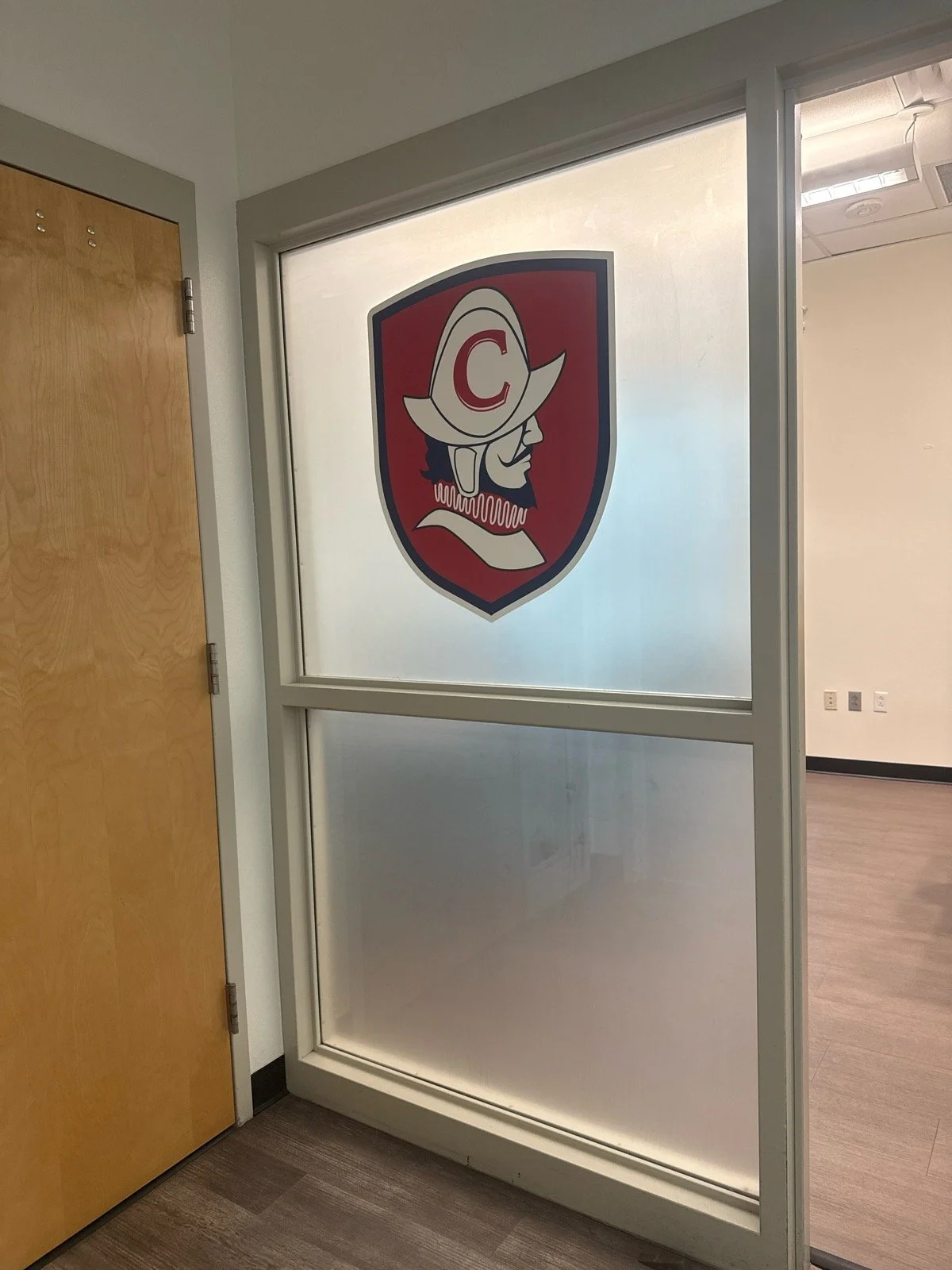A glass partition with a logo of a pirate wearing a hat with a letter 'C' on it, located in an office setting.