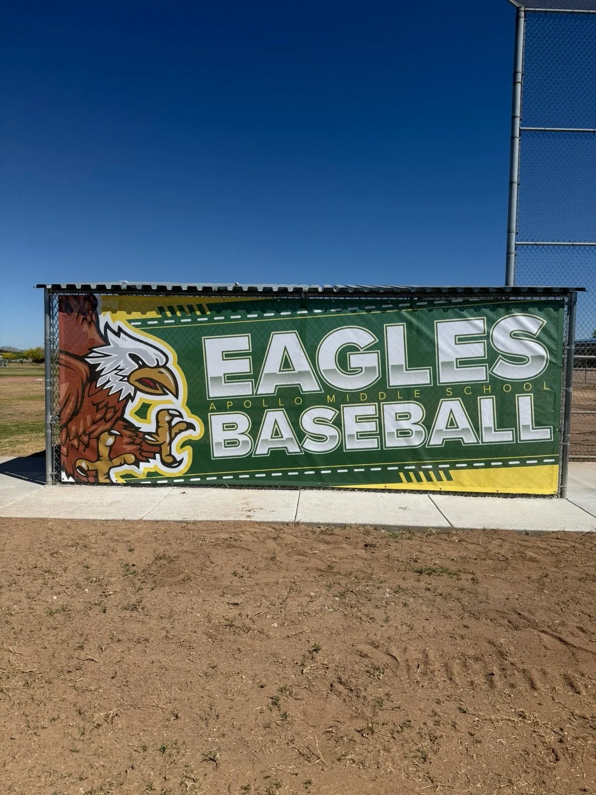 Sign for Eagle baseball team at Apollo Middle School with a graphic of an eagle, on an outdoor baseball field.