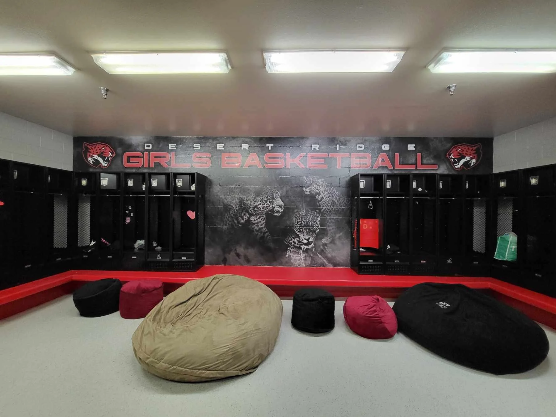 Locker room with black lockers, a large wall mural of a jaguar, and the words 'Desert Ridge Girls Basketball' in red and white. Bean bags on the floor in front of the lockers.