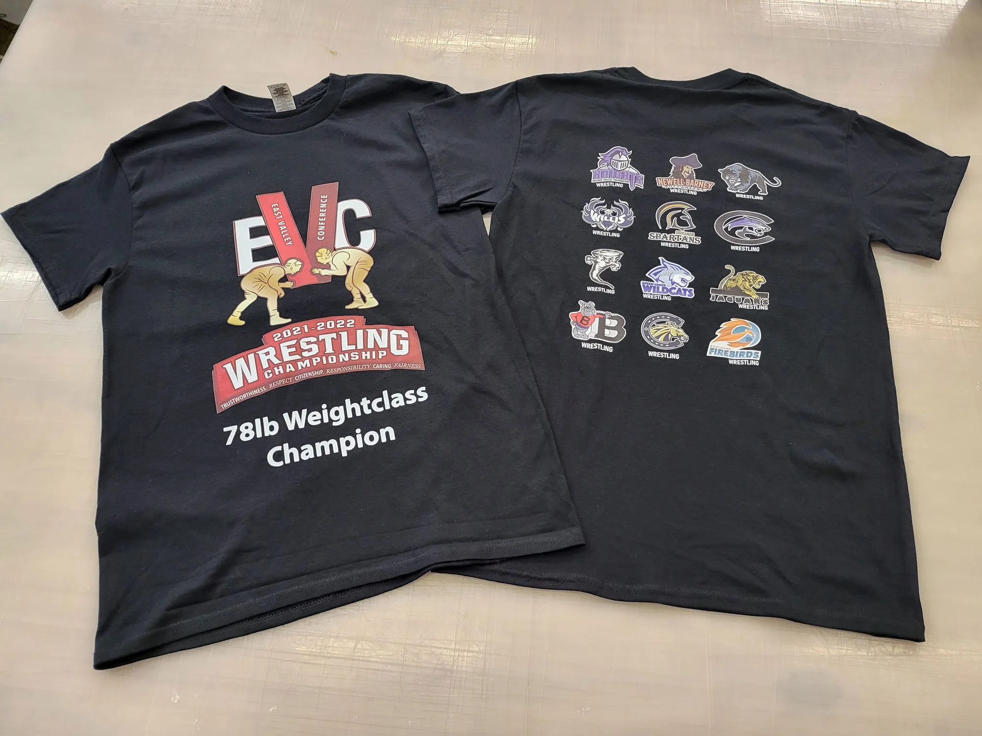 Black t-shirt with wrestling championship logo and various wrestling team logos on the back