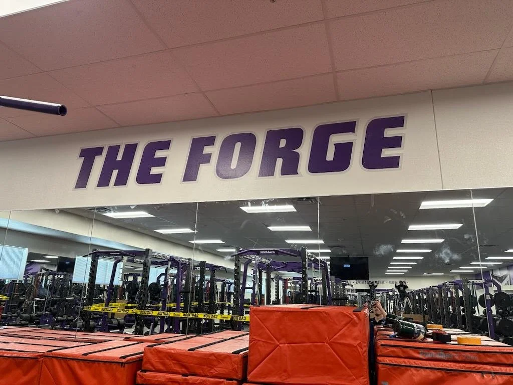 Interior of a gym called 'The Forge' with workout equipment, mirrors, and large orange padding in the foreground.