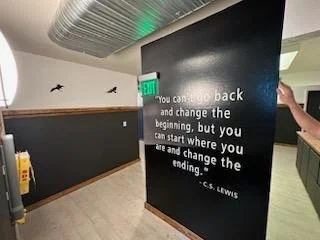 A black wall with a quote by C.S. Lewis about beginning and ending changes, and an illuminated green exit sign.