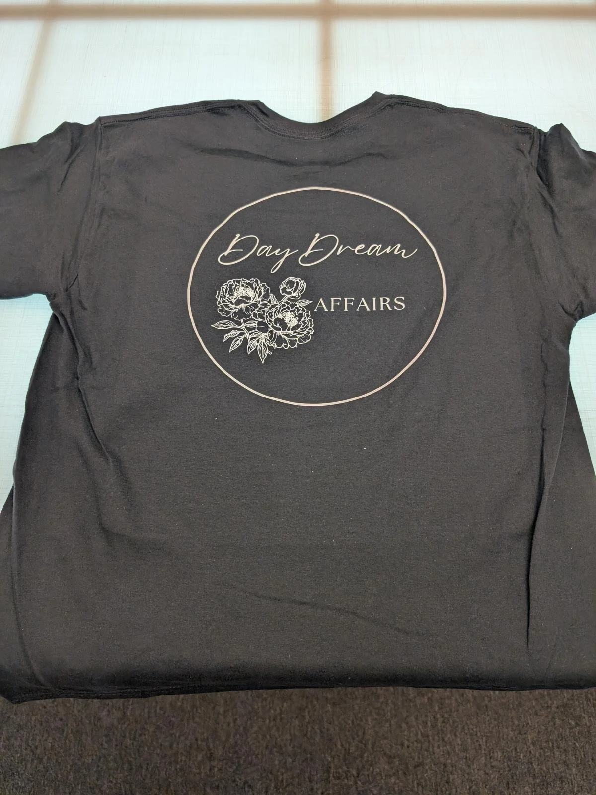 Black T-shirt with white floral logo and text that says 'Day Dream Affairs' in a circular design.