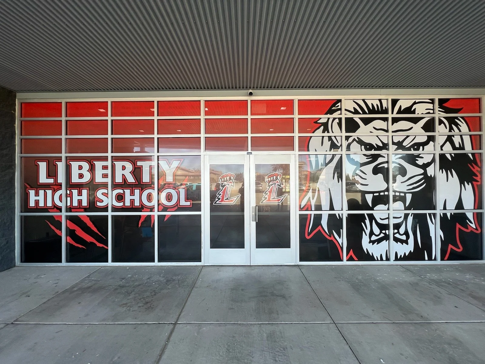 The storefront of Liberty High School with a large black, white, and red lion head graphic on the right side of the window, and the words "LIBERTY HIGH SCHOOL" in bold red and white lettering on the left side.
