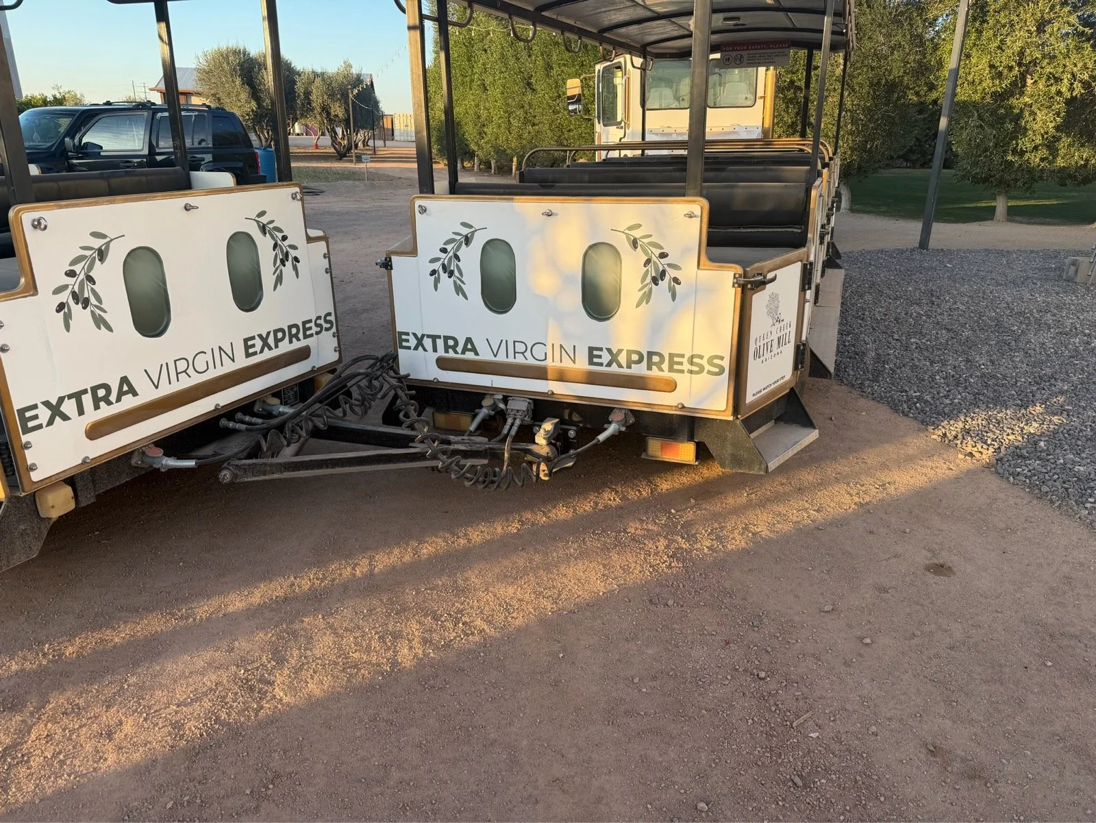 Golf cart with 'Extra Virgin Express' signs on the front and side, parked outdoors on a dirt surface.