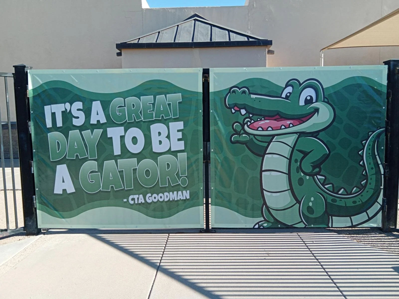 A colorful banner with a cartoon alligator smiling, wearing a friendly expression, and standing on two legs. The banner has a background of green waves and the text says: "IT'S A GREAT DAY TO BE A GATOR!" attributed to CTA Goodman.