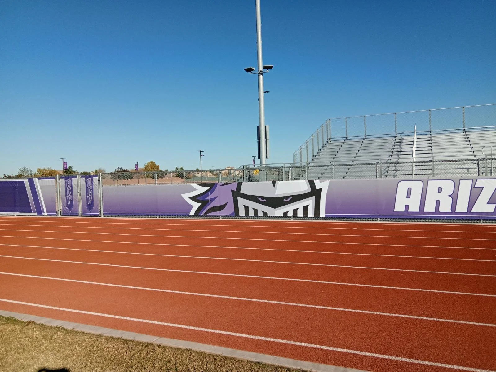 Empty outdoor sports track with a purple Arizona Wildcats banner and stadium seating in the background under a clear blue sky.