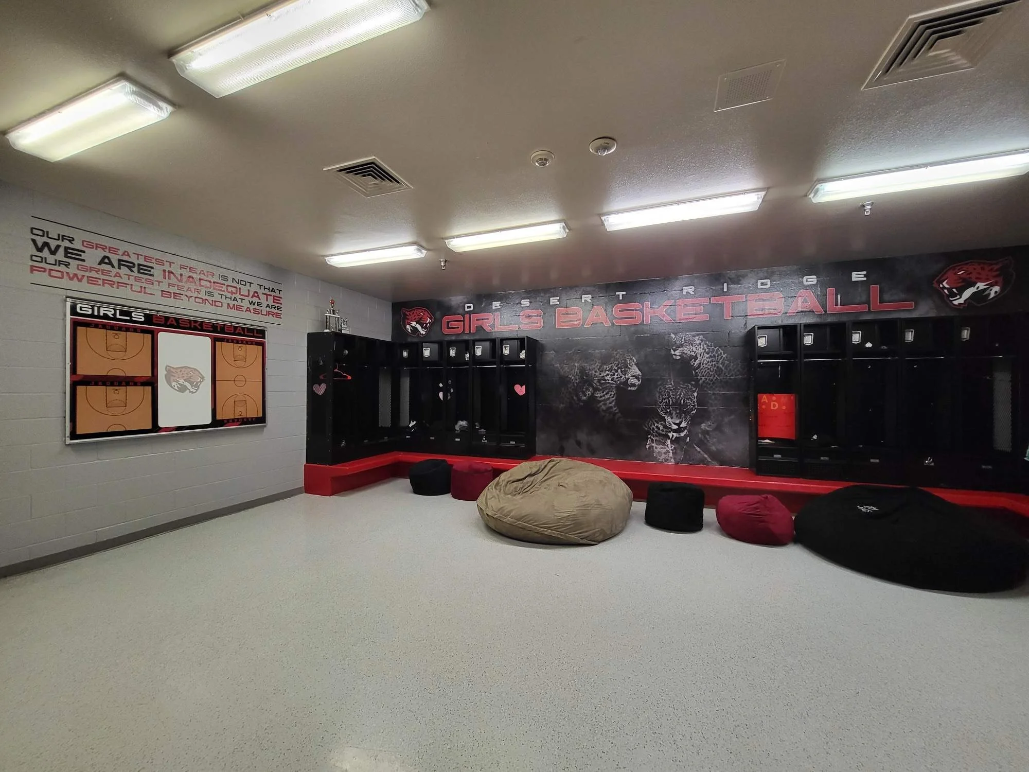 Locker room with basketball court design, large bean bags, wall decor featuring animals, and motivational text about fear and greatness.