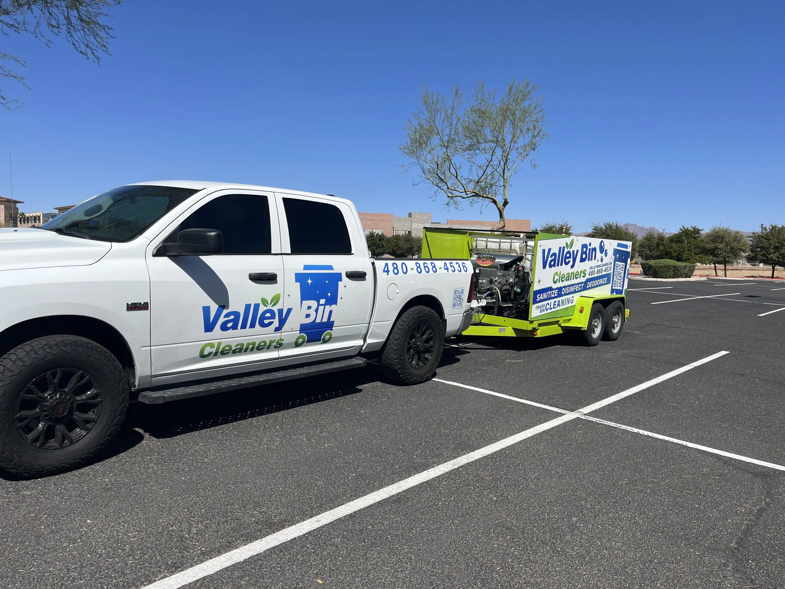 A white pickup truck with a green and white sanitation and disinfecting service logo, pulling a small green trailer in a parking lot.