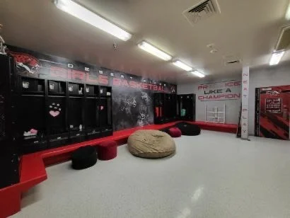 Locker room with black lockers, red benches, a beige bean bag, and red cushions, with gym equipment graphics on the walls.