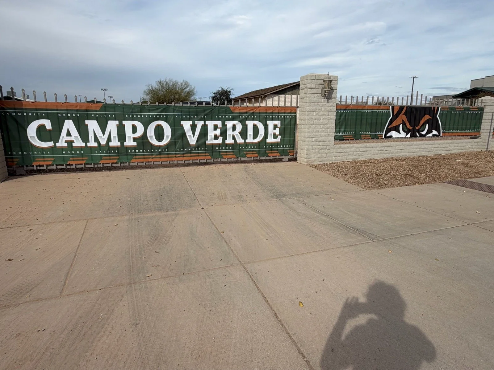 School gate with a green banner displaying 'CAMPOS VERDE', a mascot logo of an angry animal face, and a brick wall.