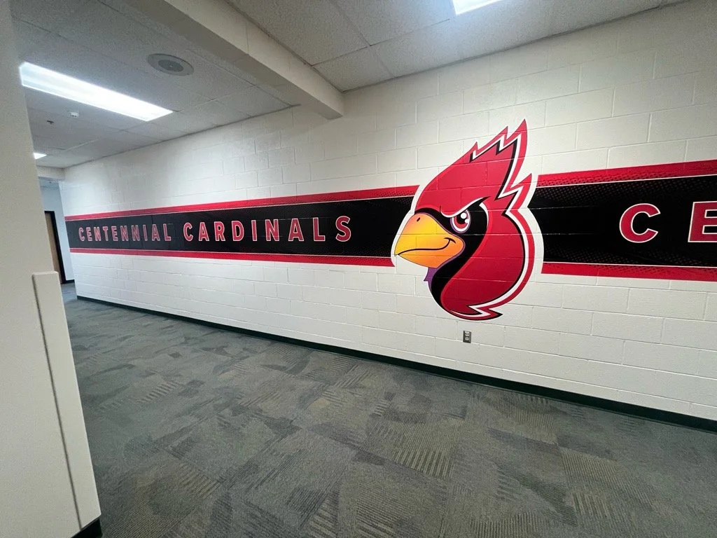 Hallway with a mural on the wall displaying the text 'Centennial Cardinals' and a large cartoon cardinal mascot with a yellow beak and red feathers.