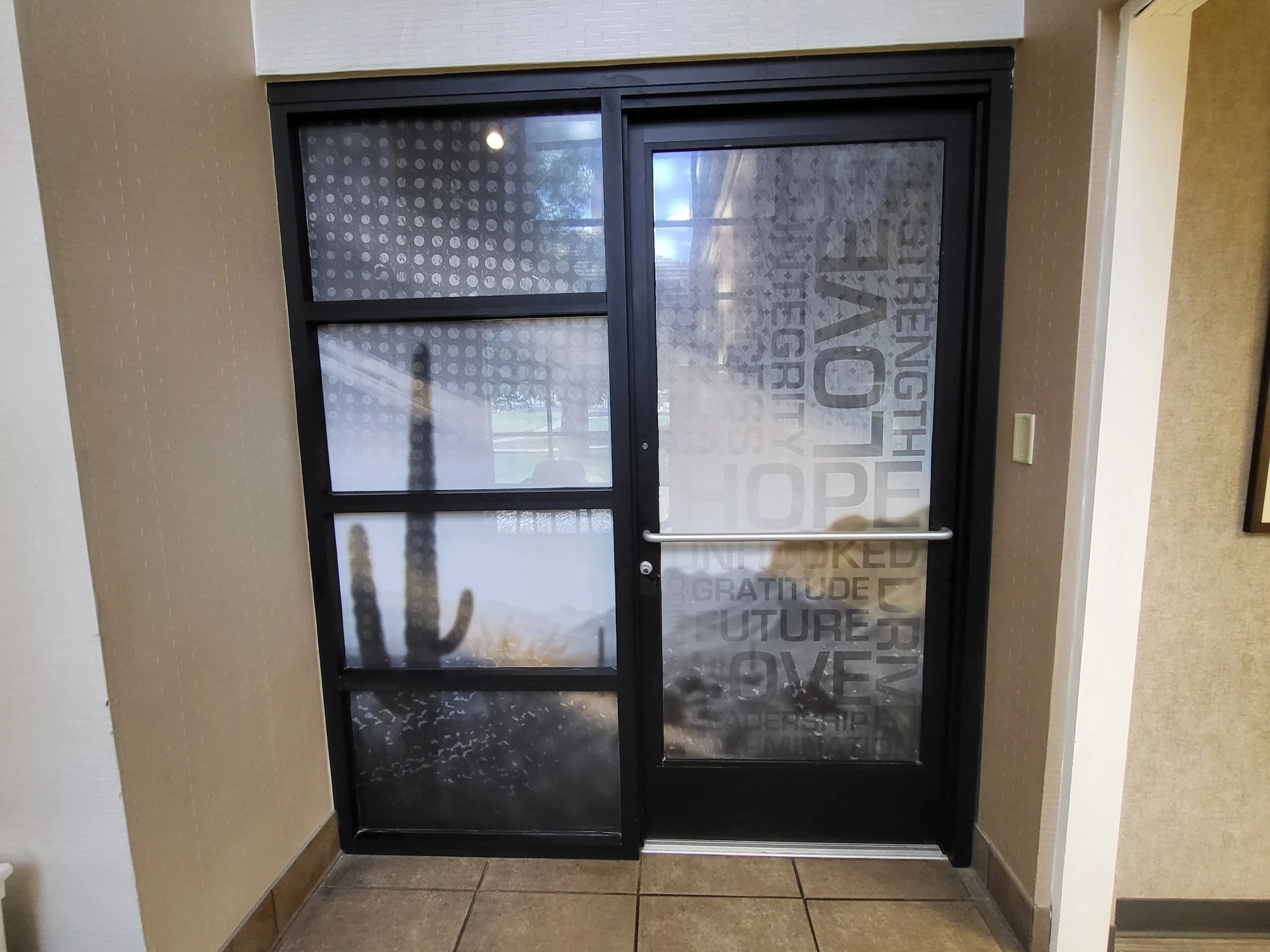 Entrance door made of glass with words like Love, Hope, Gratitude, and Unity printed on it, inside a building.
