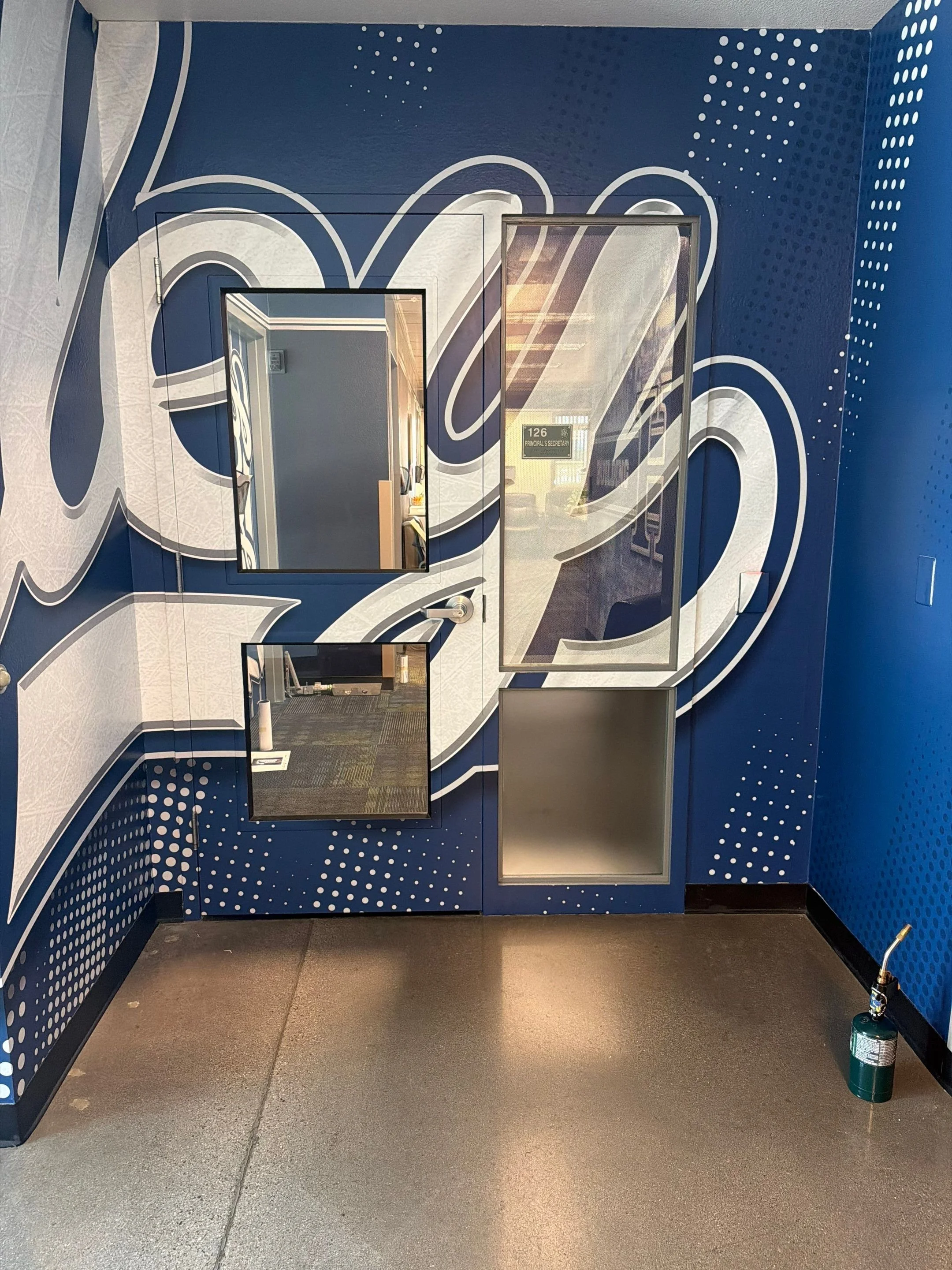 Interior view of a blue and white decorated wall with three mirrors and a fire extinguisher on the floor in front of the wall.