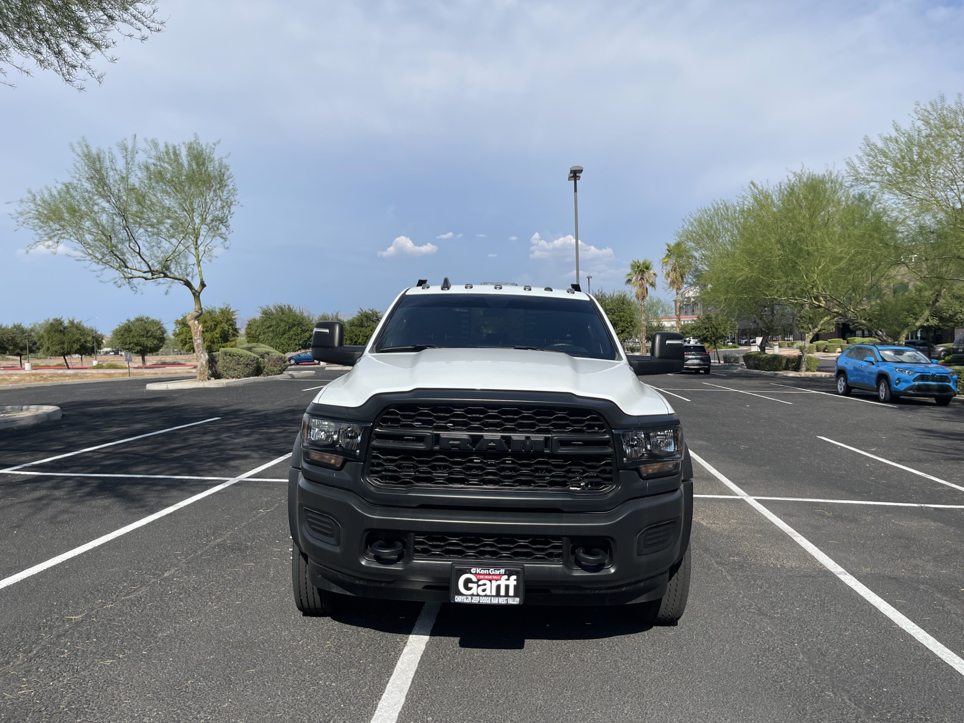 Front view of a black RAM truck in a parking lot, with a dealership plate that reads Garff, and several trees and parked cars in the background.