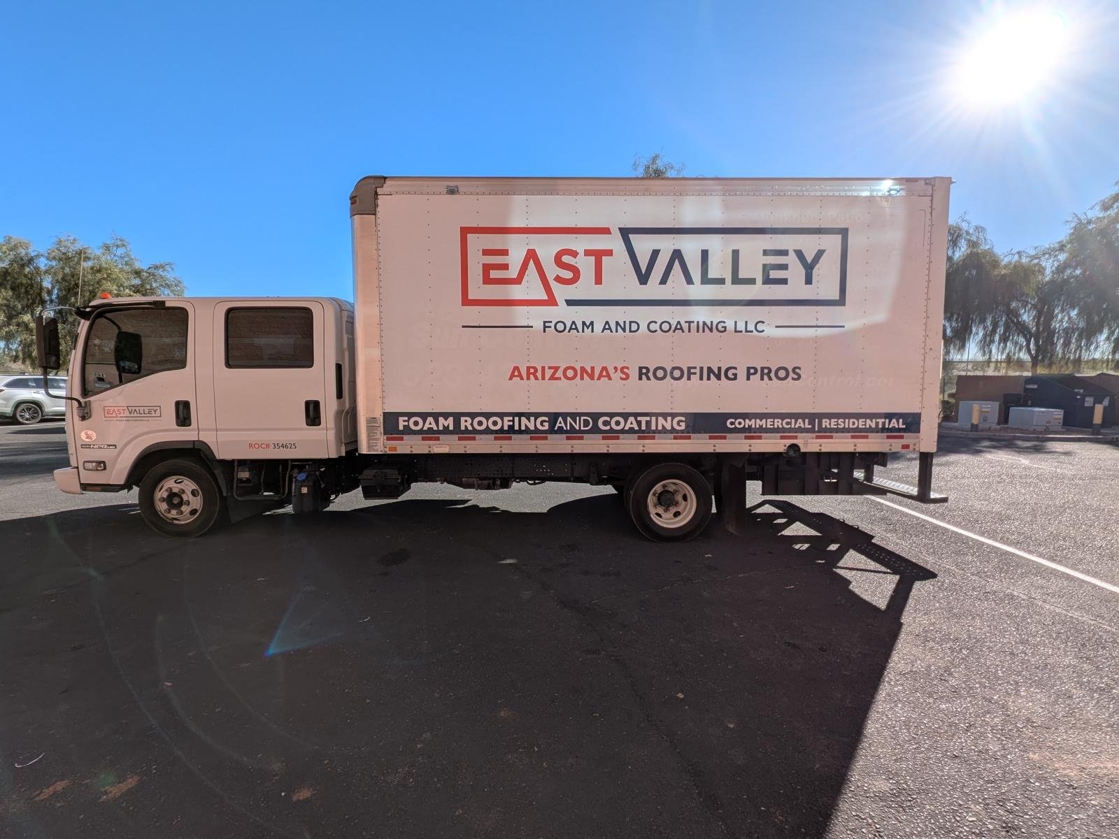 A white truck with company branding for East Valley Foam and Coating LLC parked in a parking lot, with clear blue sky and trees in the background.