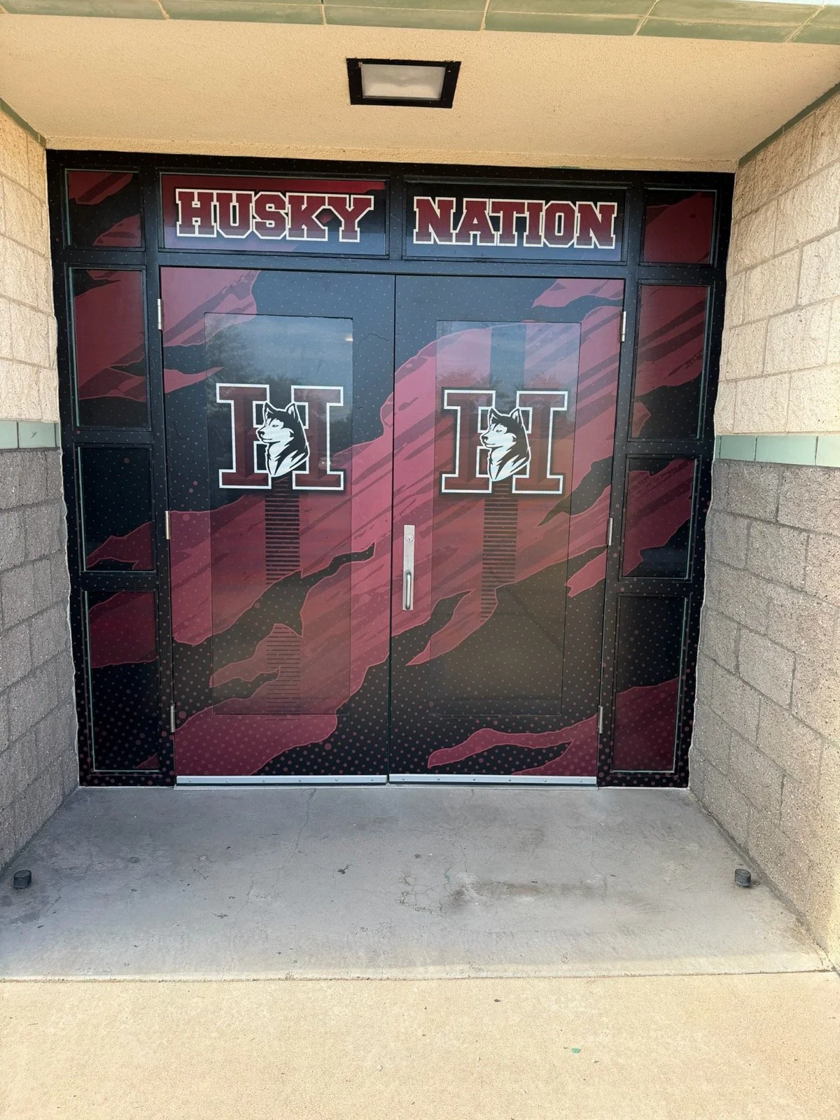 Double doors with Husky Nation theme, featuring Husky logos with a husky's head in front of a large letter 'H,' and a background with dark red, black, and maroon abstract patterns.