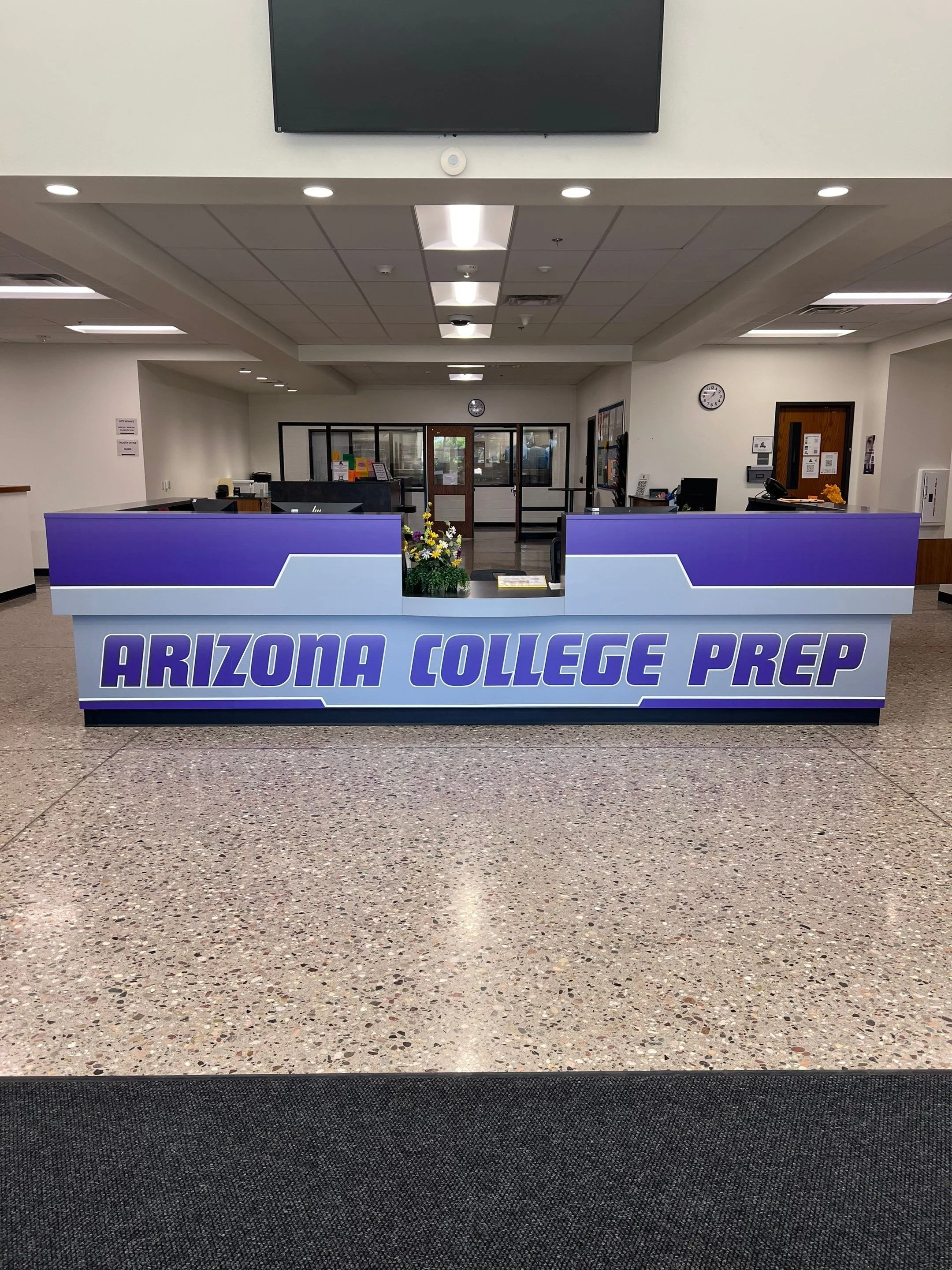 Reception desk for Arizona College Prep with purple and light blue colors, a flower arrangement, and a sign that says 'Arizona College Prep'.