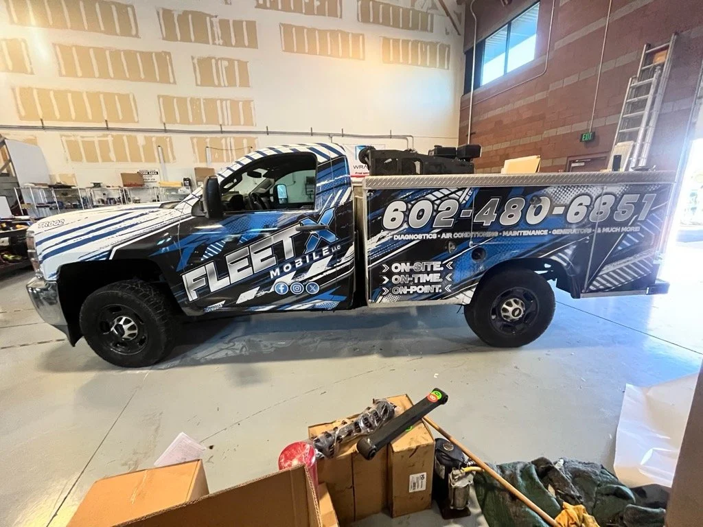 Black and blue service truck with FLEET MOBILE LLC branding, contact number, and services listed, parked inside a warehouse or garage.