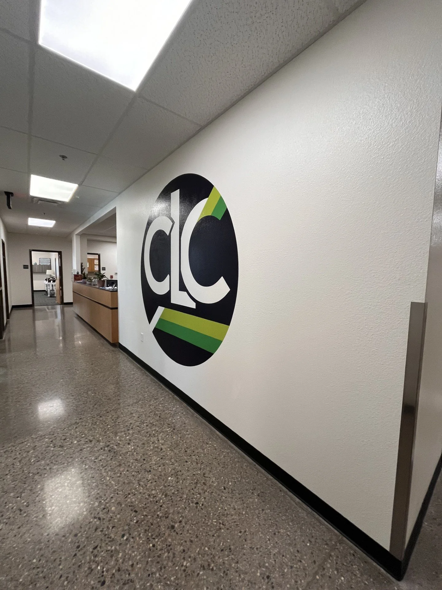 Hospital corridor with a white wall, a large circular logo with 'CLC' letters, and a reception desk.