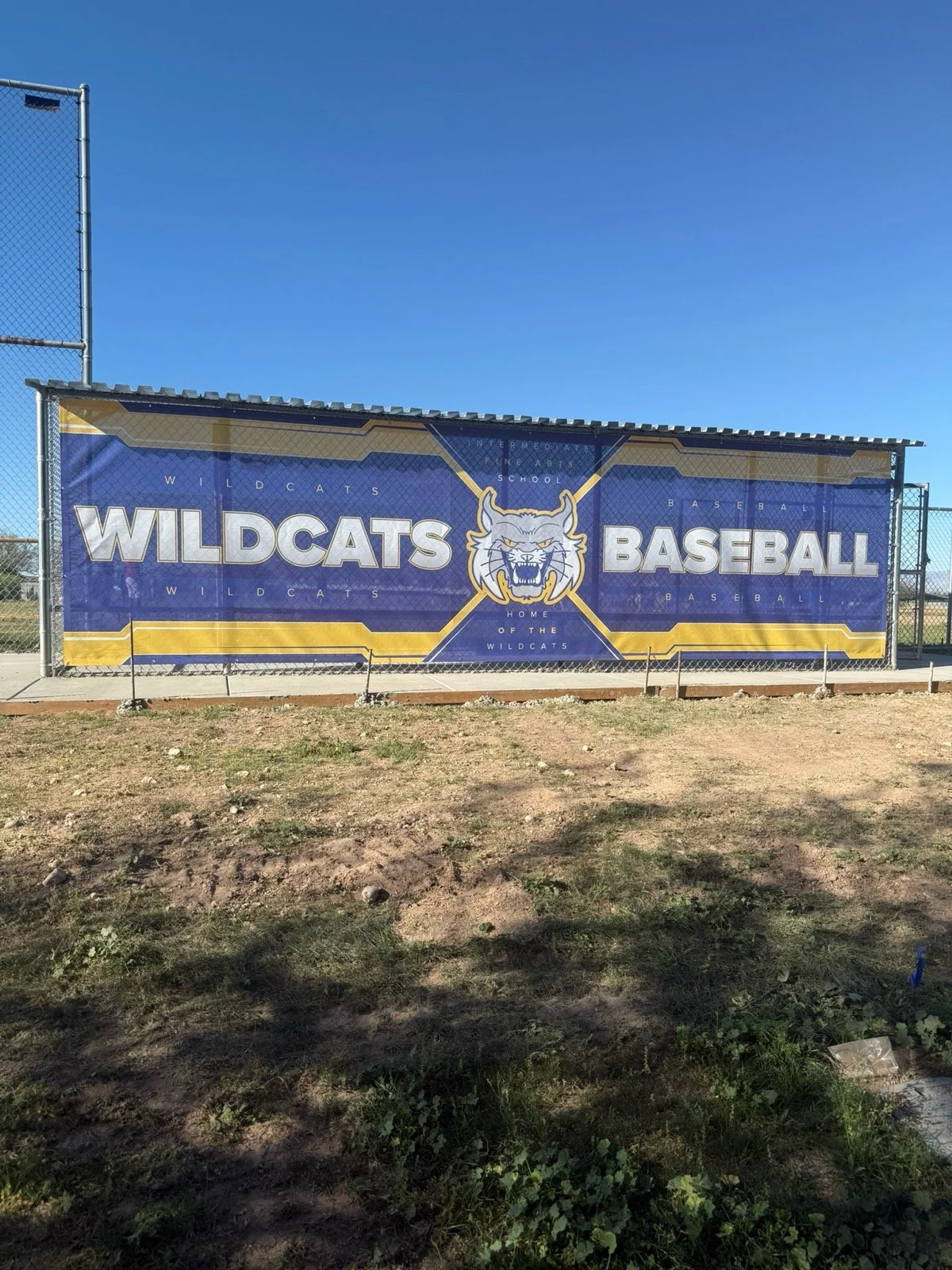 A large blue and yellow banner on a chain-link fence promoting Wildcat baseball, featuring a wildcat head logo in the center.