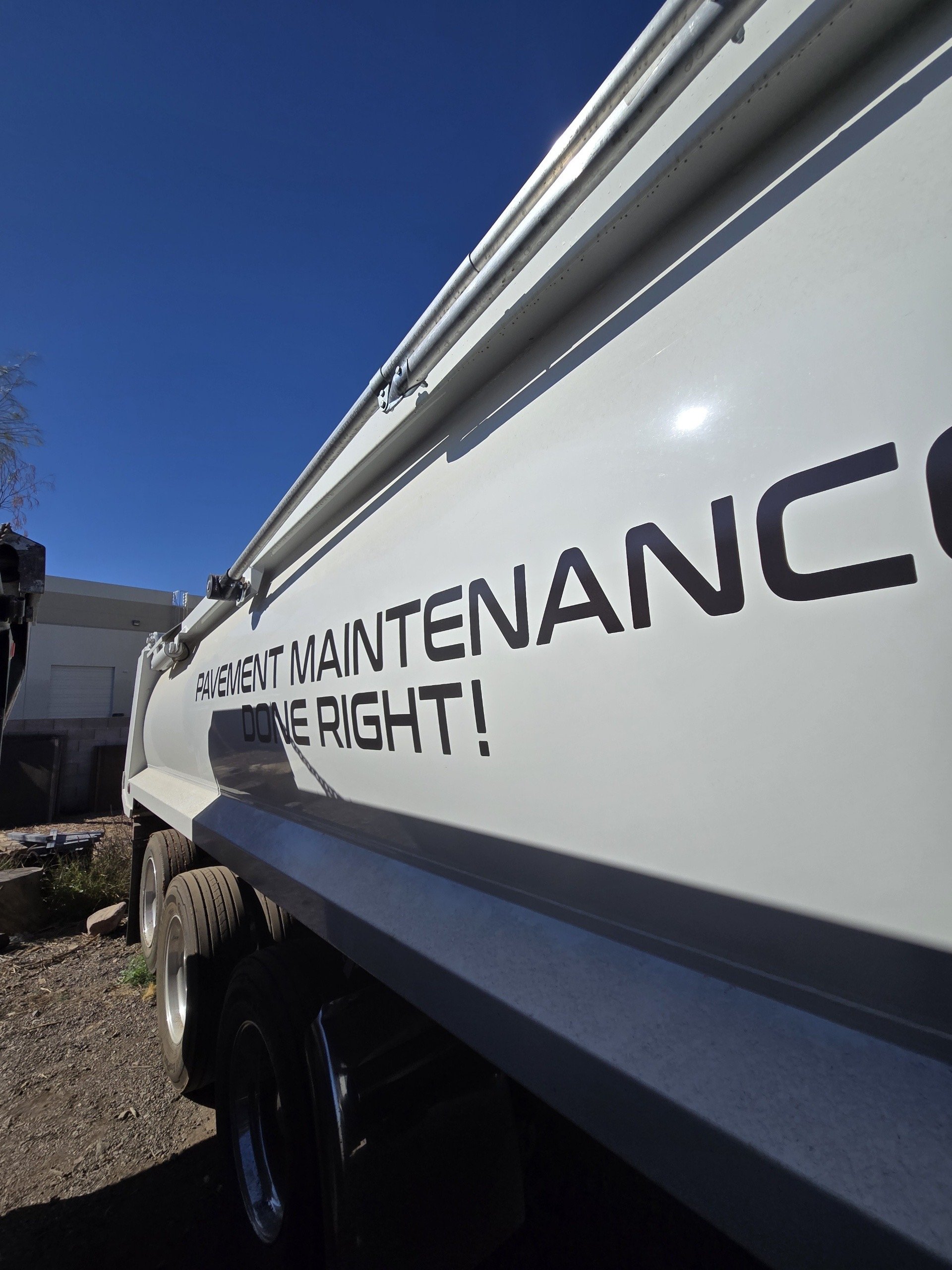 Close-up of a vehicle with a white sign that reads 'PAVEMENT MAINTENANCE DONE RIGHT.' in black text, parked outdoors under a clear blue sky.
