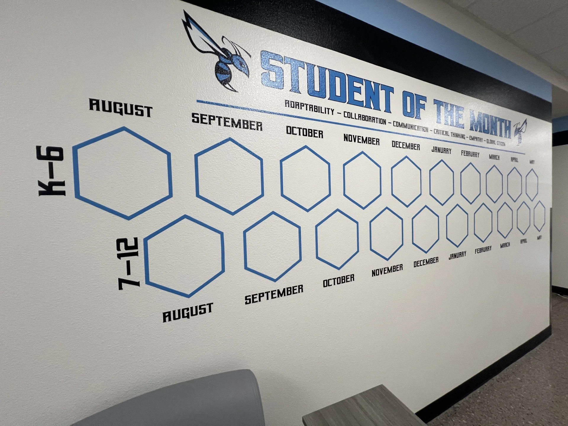 A classroom wall display titled 'Student of the Month' with a honey bee logo, featuring months from August to May, each with empty hexagon spaces for student names.