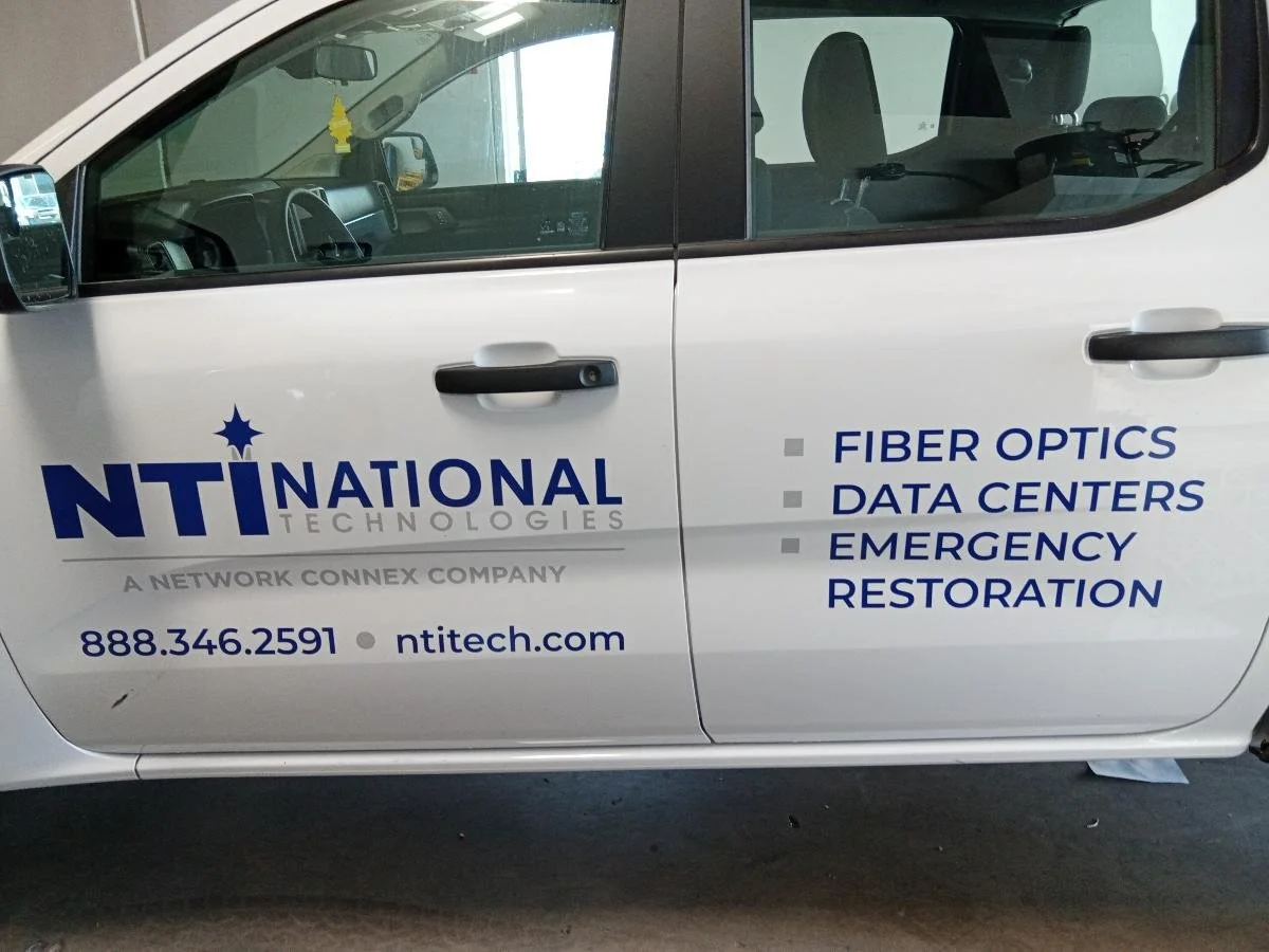 Side view of a white company's service vehicle displaying logo and services for NTIATIONA; Technologies, including fiber optics, data centers, and emergency restoration.