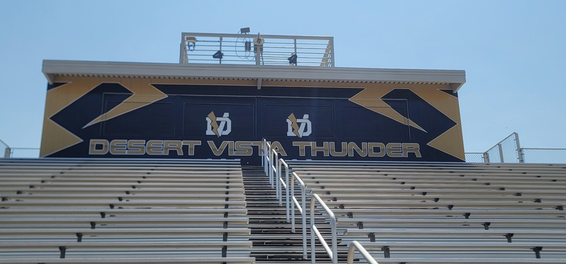 The stadium sign reads 'Desert Vista Thunder' with a black and gold color scheme and lightning bolt graphics, seen from the bleacher stairs on a clear day.