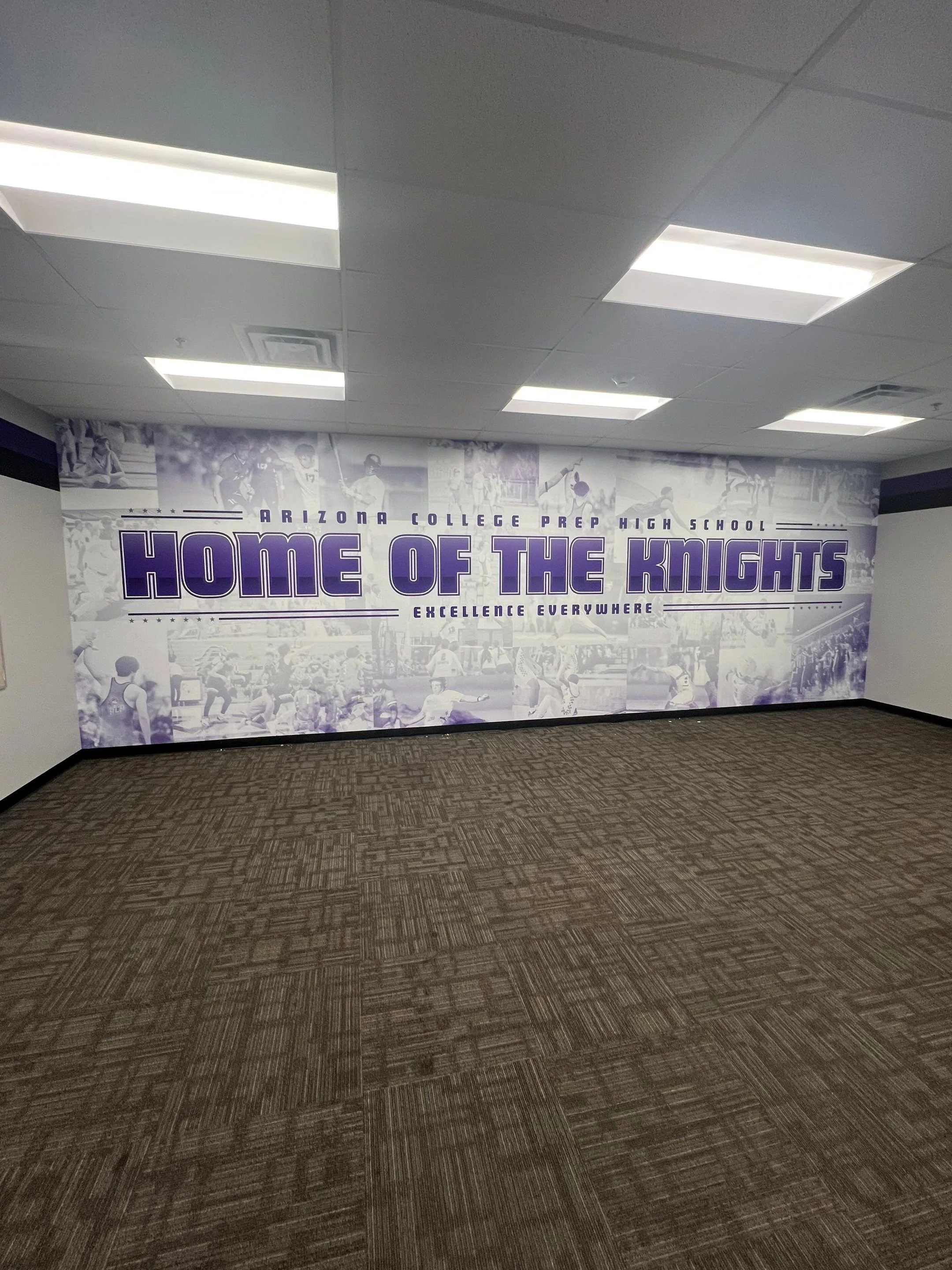 A large wall mural with the text 'Arizona College Prep High School' and 'Home of the Knights' in purple, featuring black-and-white images of students participating in sports and school activities, in an indoor hallway with carpeted floor and ceiling 