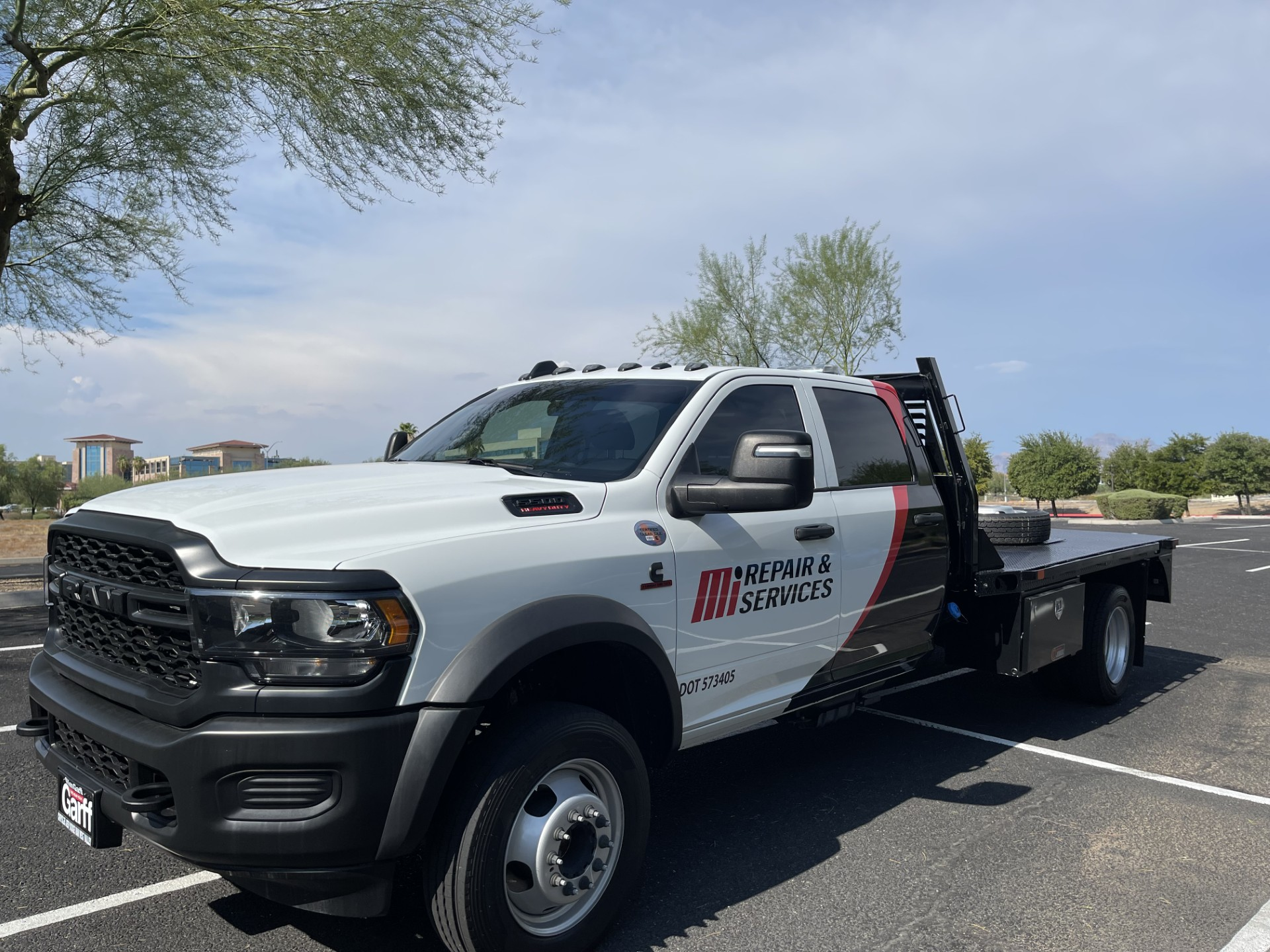 A white tow truck parked in a parking lot under a partly cloudy sky, with some trees and buildings in the background.