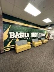School hallway with a mural that reads 'Basha High School' and features green and yellow colors, with yellow benches in front of it.