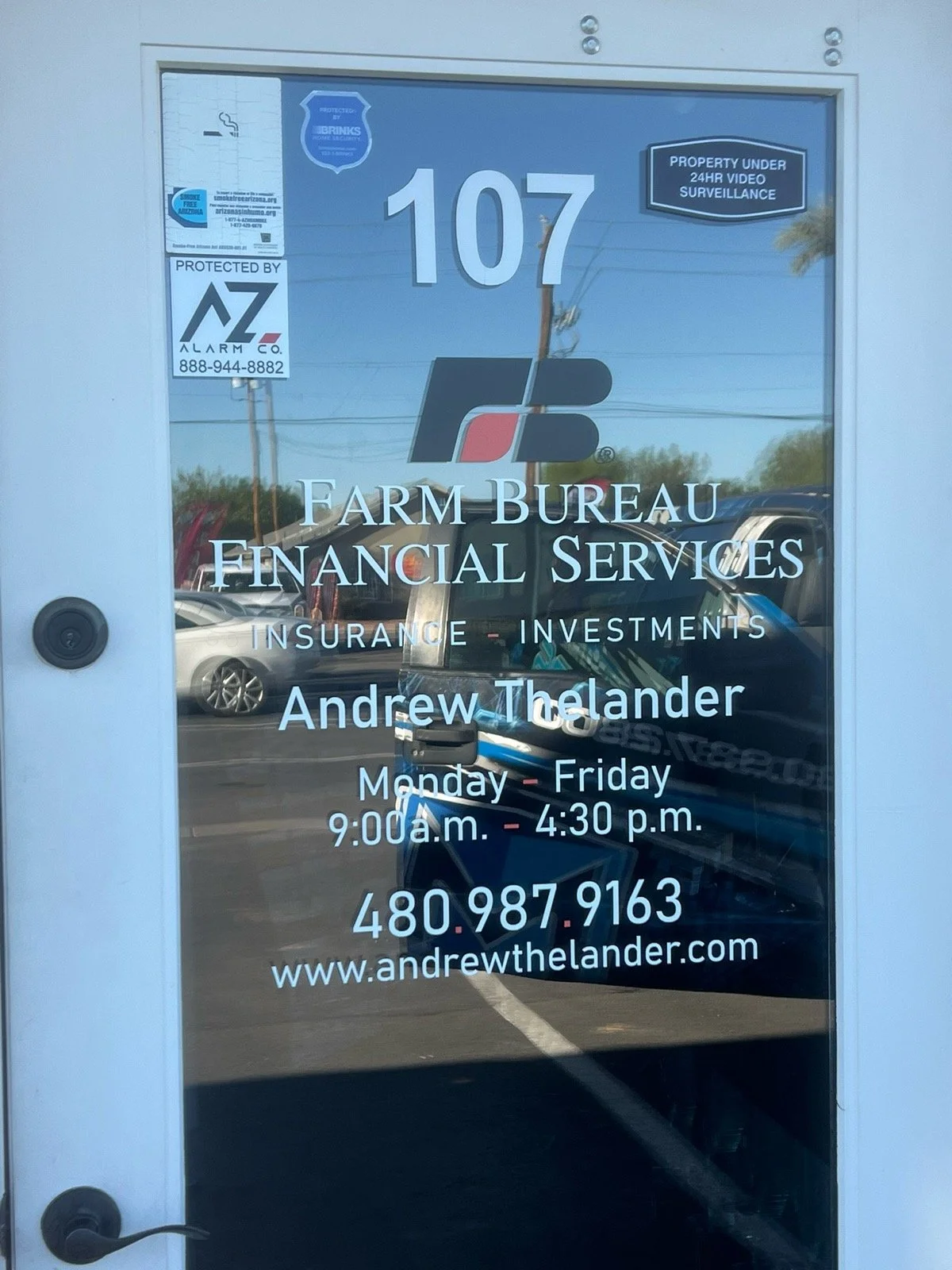 Glass door of Farm Bureau Financial Services office with contact information, operating hours, and signs indicating property under video surveillance and protection by AZ Alarm Co.