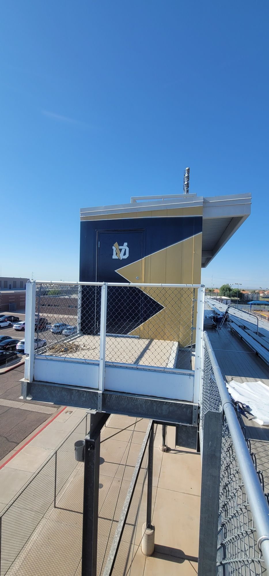 View from a rooftop parking lot showing a stairwell with a mural of a coffee cup and arrow signs on the side of a building, parking lot below, and a clear blue sky.