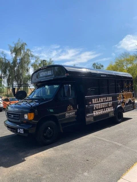 Black rescue vehicle with a firefighter logo and banners reading 'Relentless Pursuit of Excellence' parked in a lot under a blue sky with trees in the background.