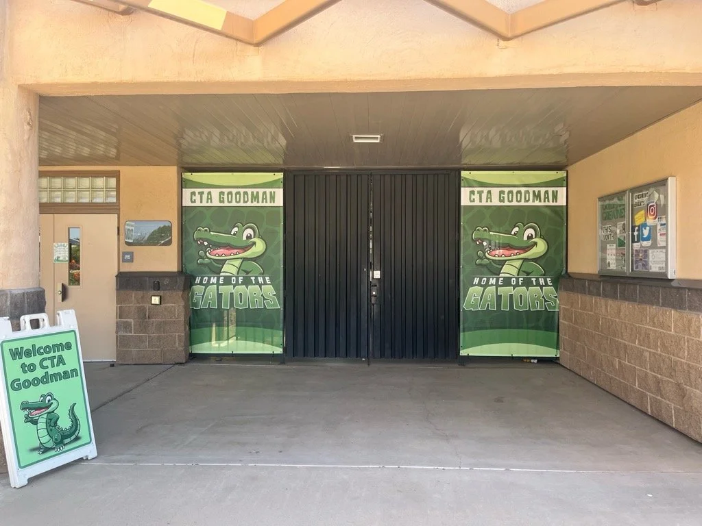 Entrance to a school or community center with banners and a sign featuring a cartoon gator mascot called the Gators, welcoming visitors to CTA Goodman.
