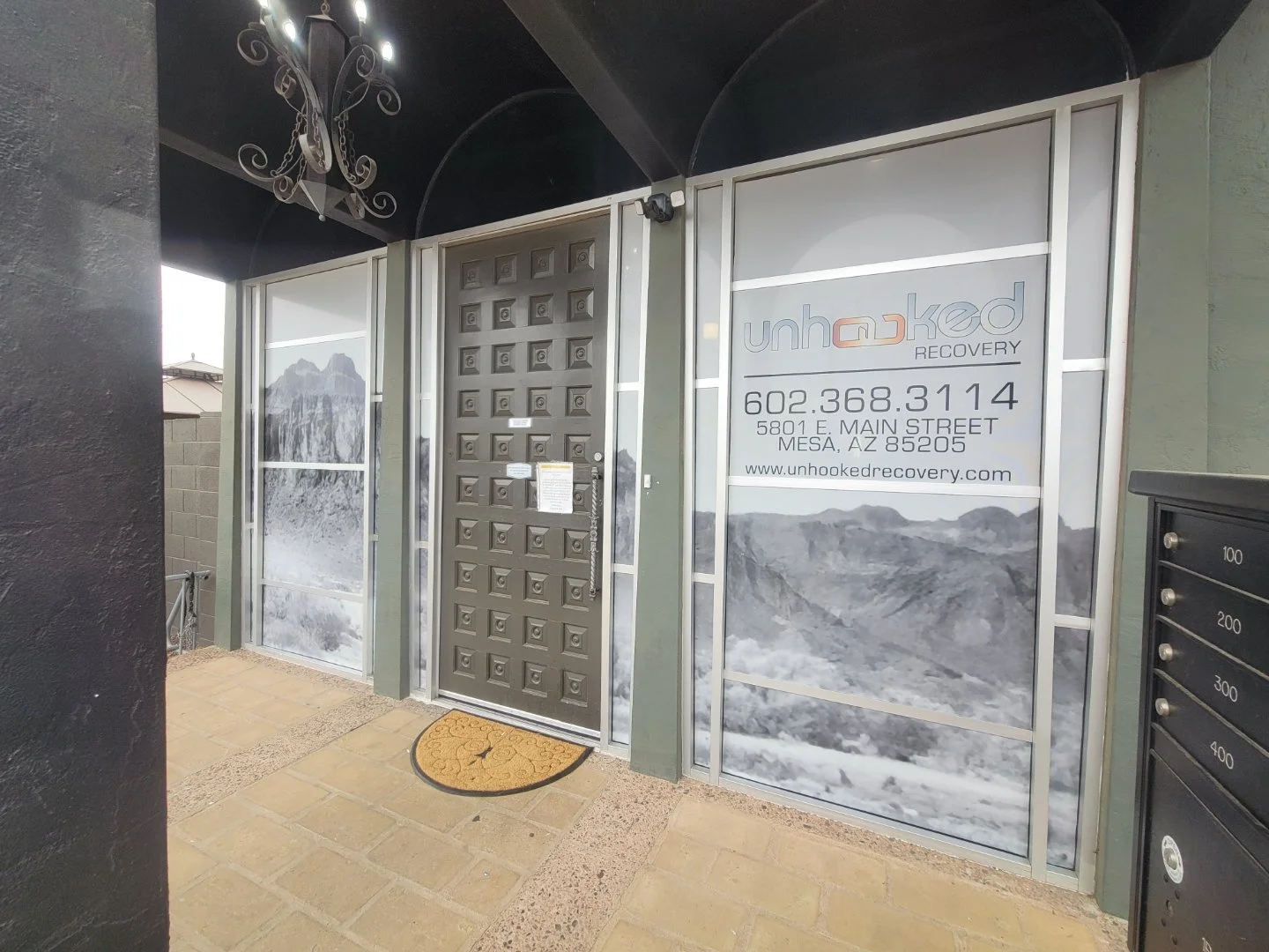 Entrance to Unhooked Recovery with a metal door, business information on windows, and a mountain landscape in the background.