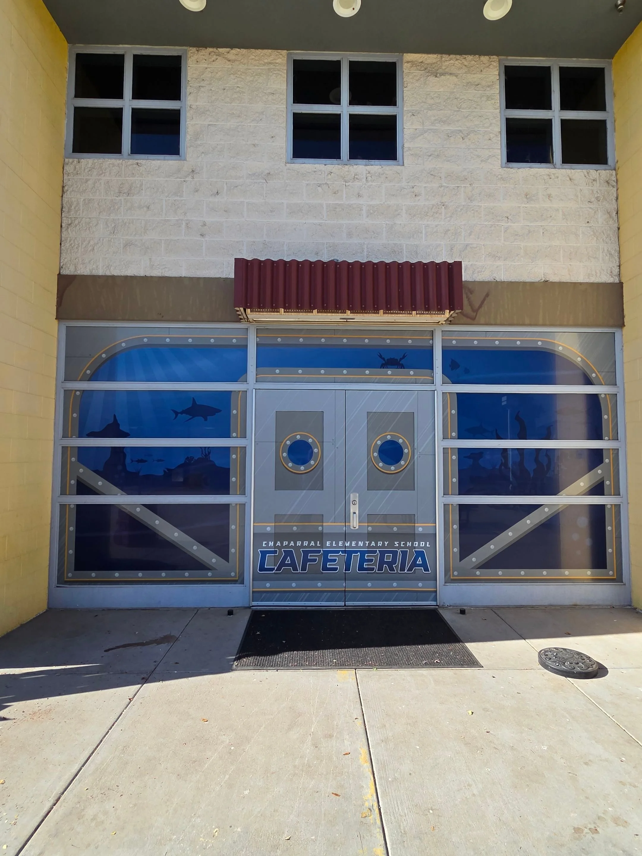 Entrance to Chaparral Elementary School cafeteria with a large, decorated door featuring images of sharks and ocean fish, and the school name displayed.