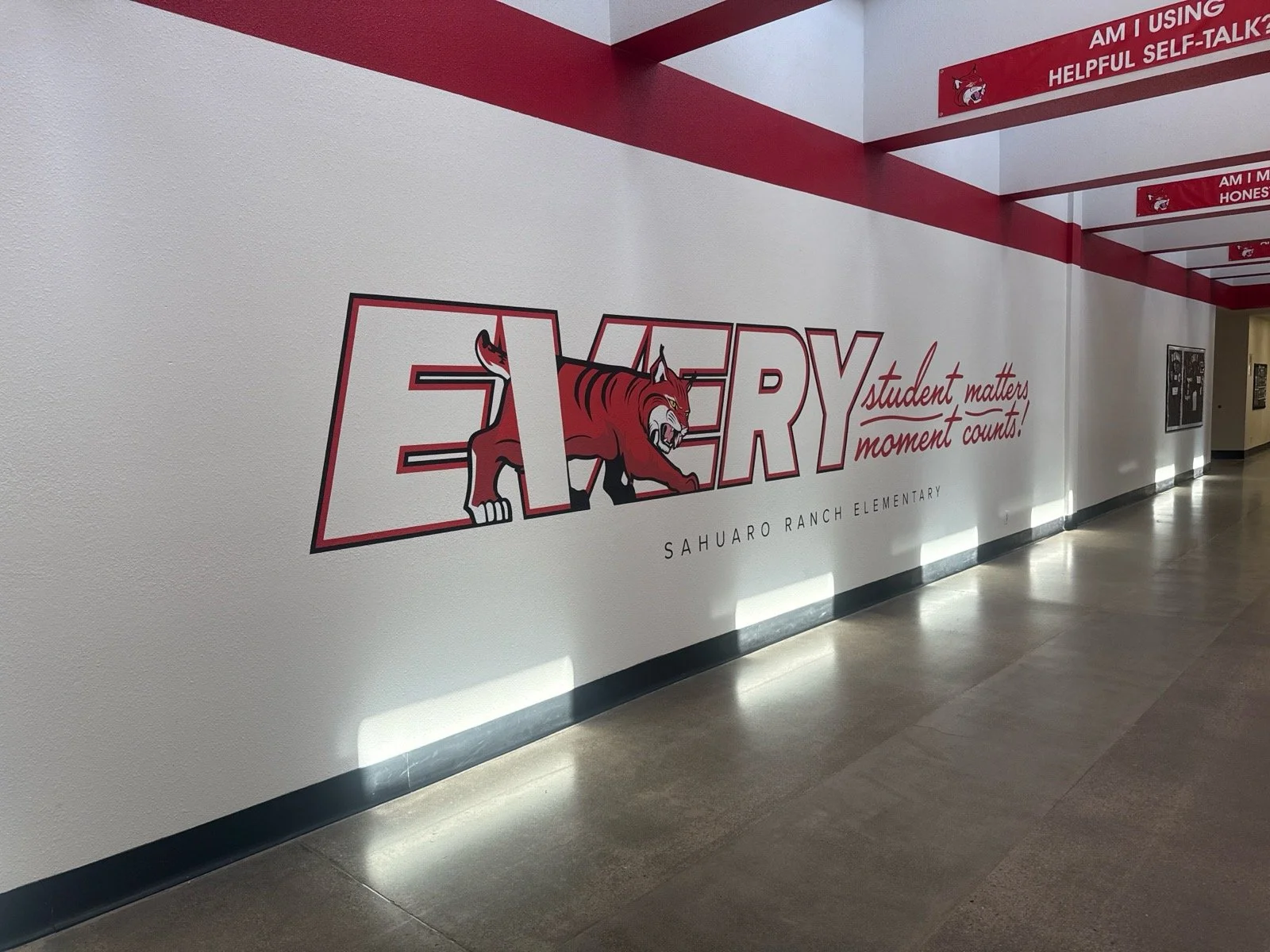 School hallway wall with a large mural featuring a red and white school mascot, a tiger, inside the word 'EVERY'. The mural includes the slogan 'student matters, moment counts!' and the school name 'Sahuaro Ranch Elementary' underneath.